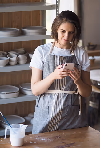 Portrait d'une femme artisan céramiste en train de regarder son logiciel de gestion financière sur son téléphone