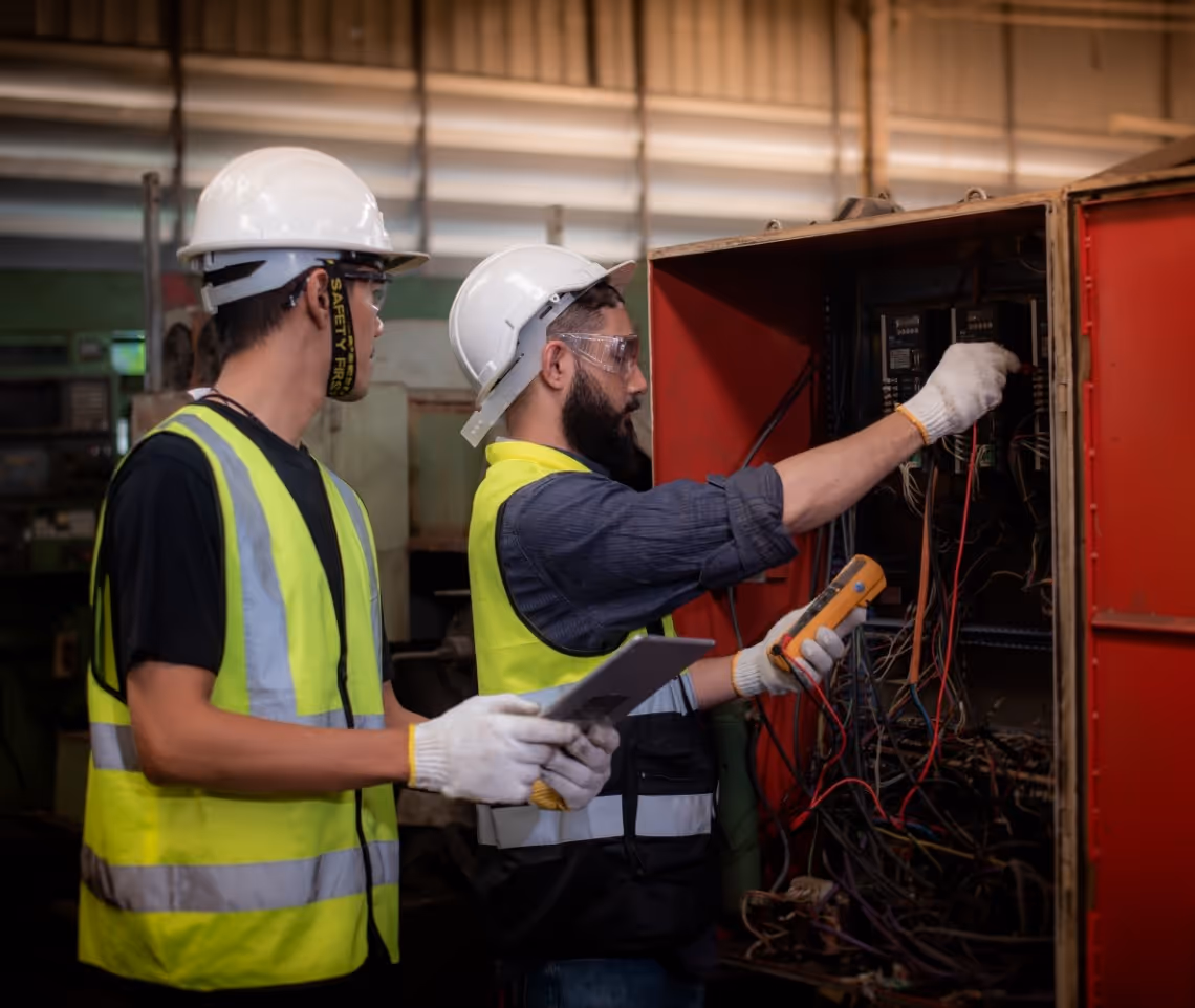 Electrical technicians in safety gear checking wiring in industrial electrical panel