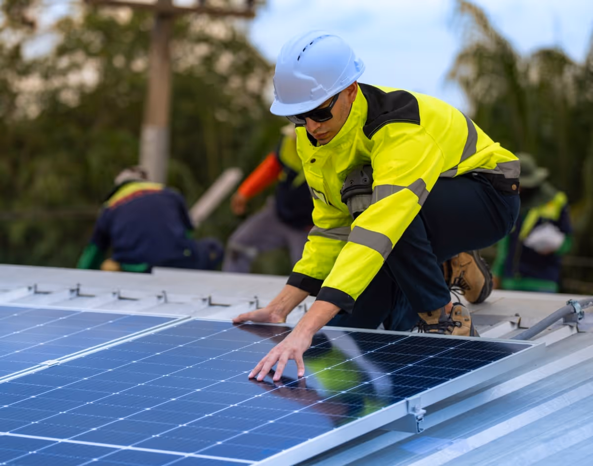 Worker in safety gear installing solar panels on rooftop