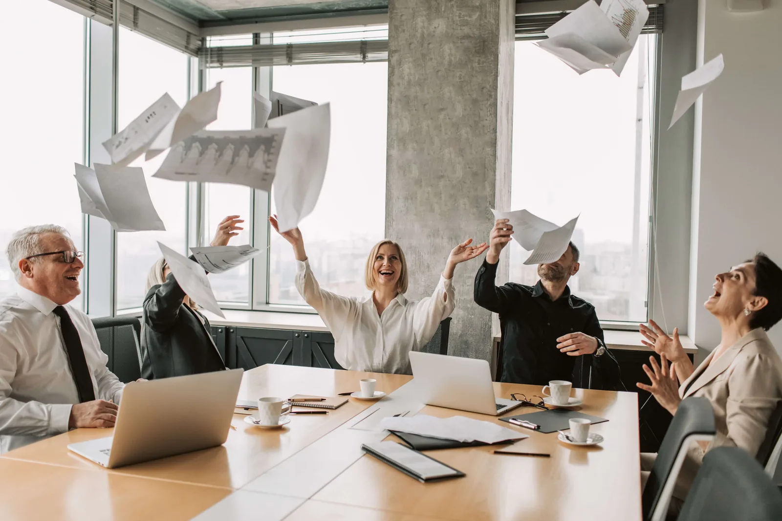 a group of people sitting around a table throwing paper in the air