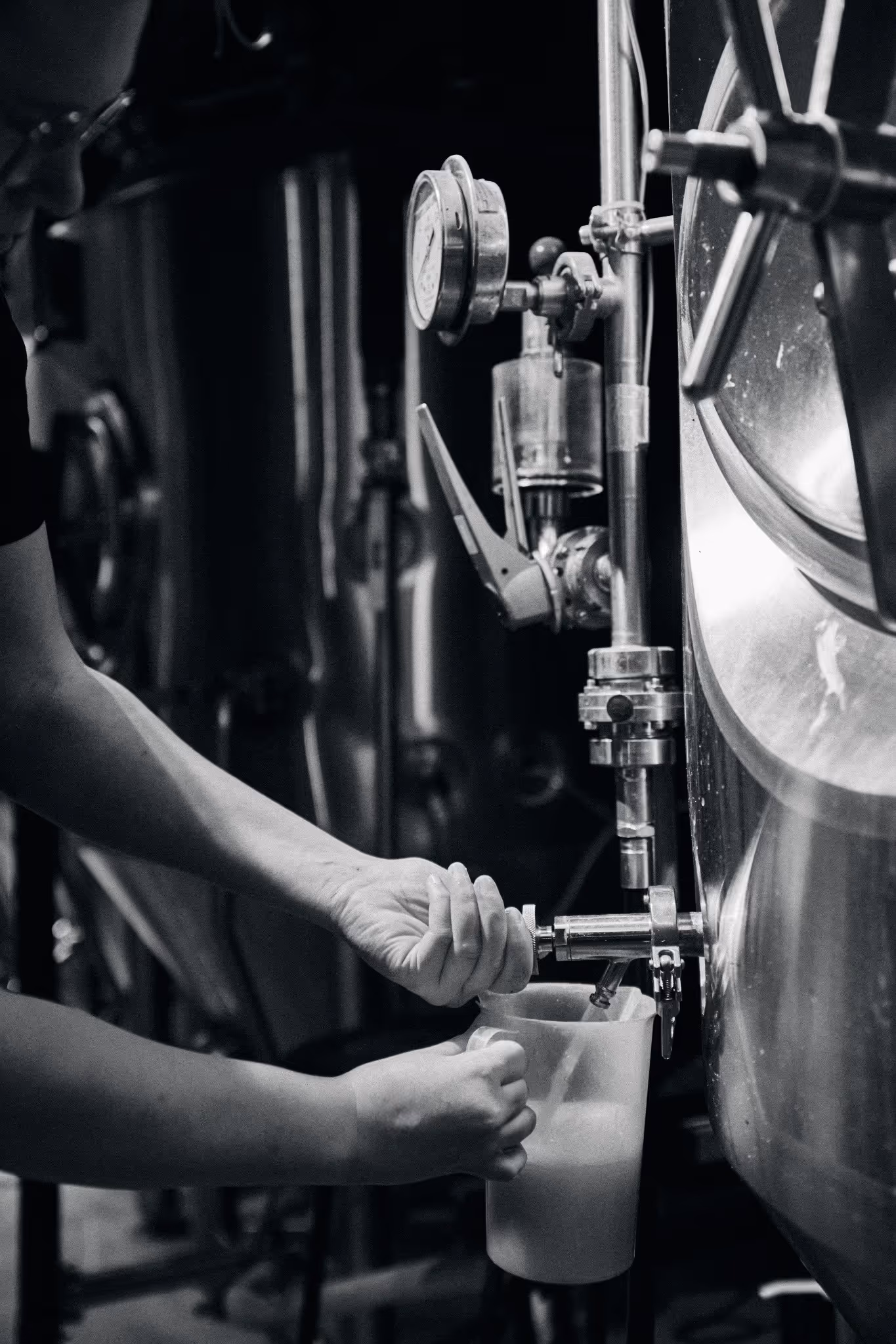 Persoon die vloeistof uit een roestvrijstalen tank aftapt in een maatbeker in een brouwerij.