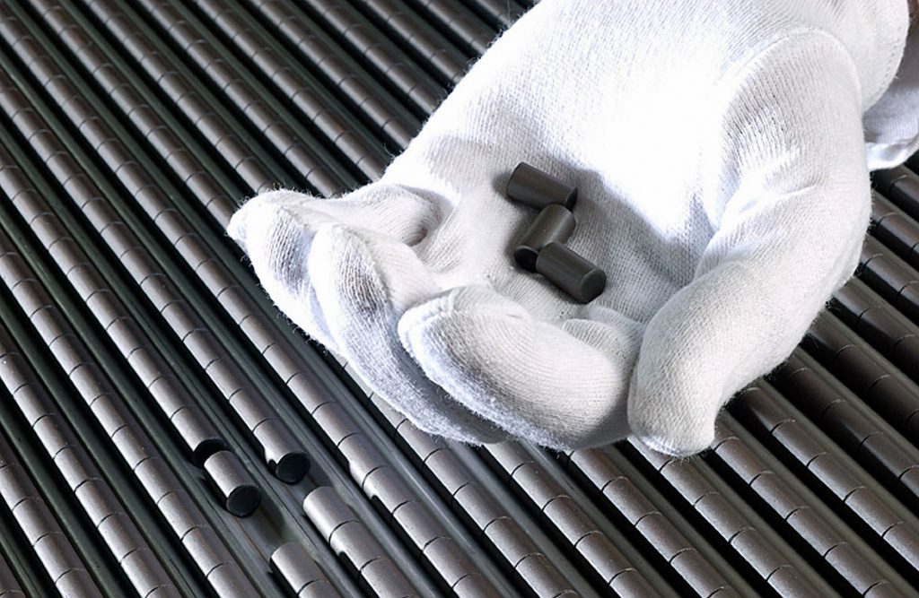 A white-gloved hand holds three uranium pellets prior to being encased in a nuclear fuel rod.