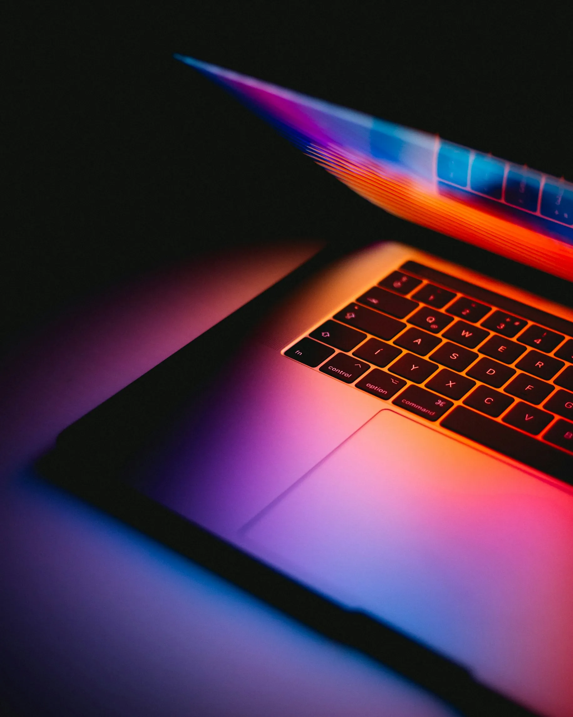 Close-up of a laptop keyboard and partially open screen glowing with colorful red, purple, and blue light.