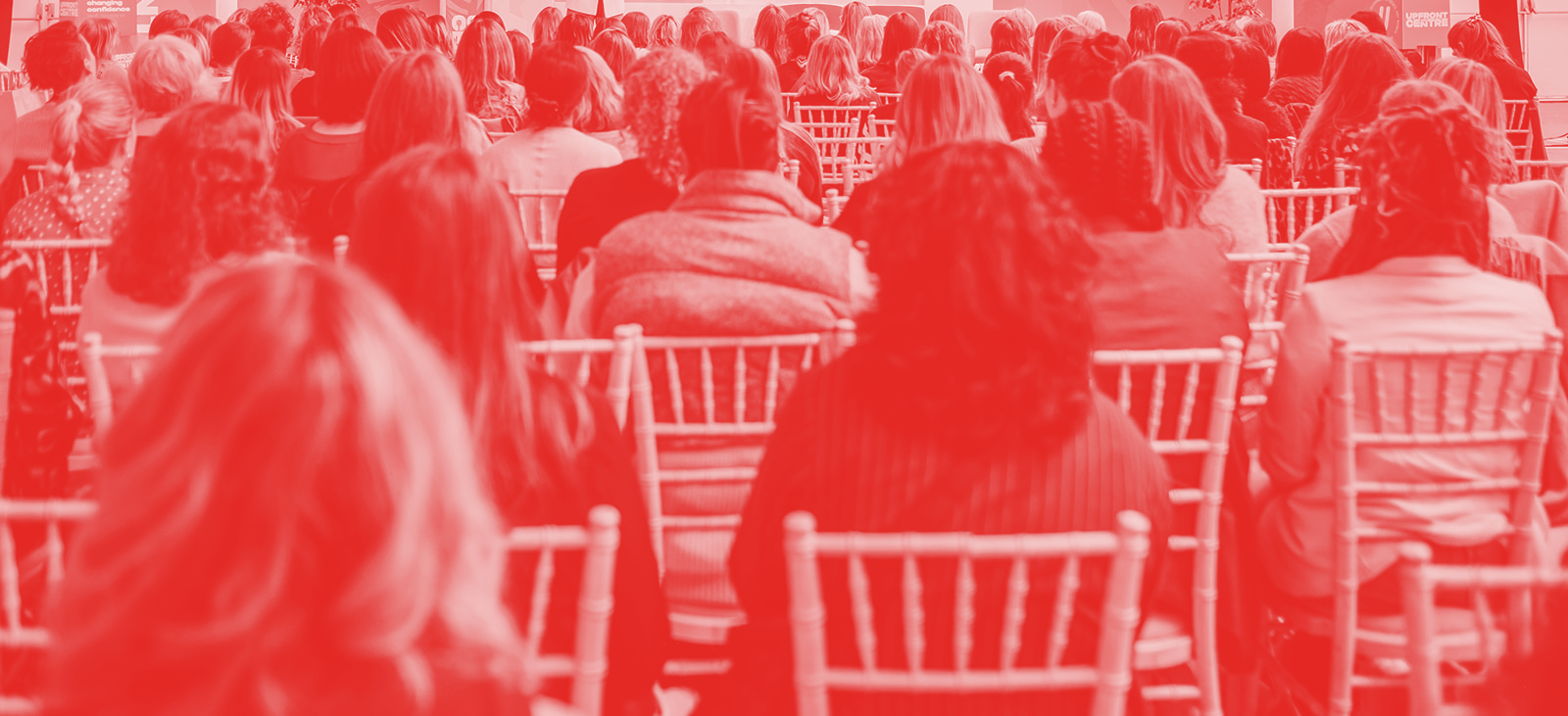 Image of women sitting in chairs looking at the stage of an UPFRONT conference, image is coloured red
