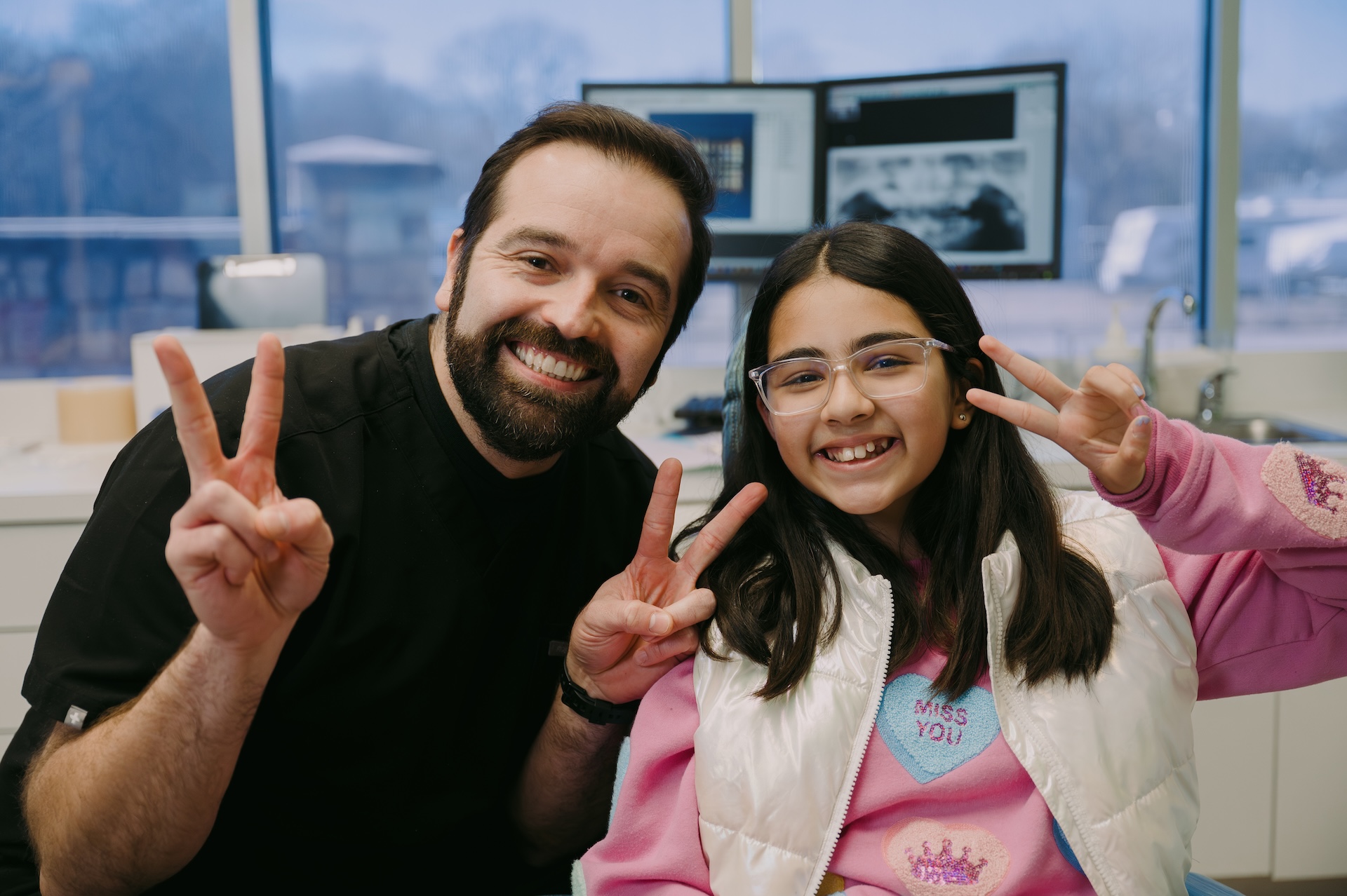Dentist and smiling young patient flash peace signs at Just For Kids Dental.