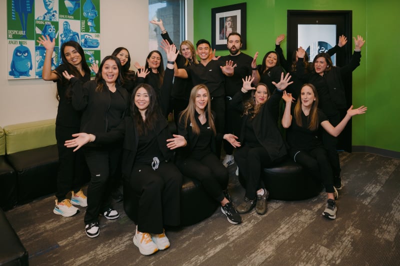 Dental team of multiple staff members in black uniforms standing together in office with colorful wall art