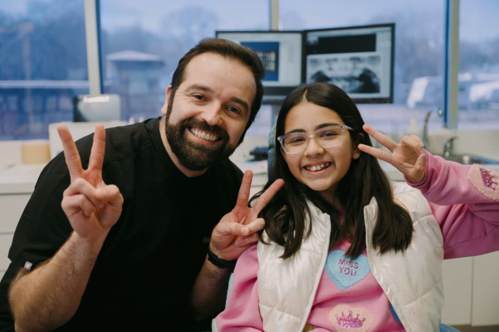 Male dentist with child patient making peace sign gesture together, both smiling