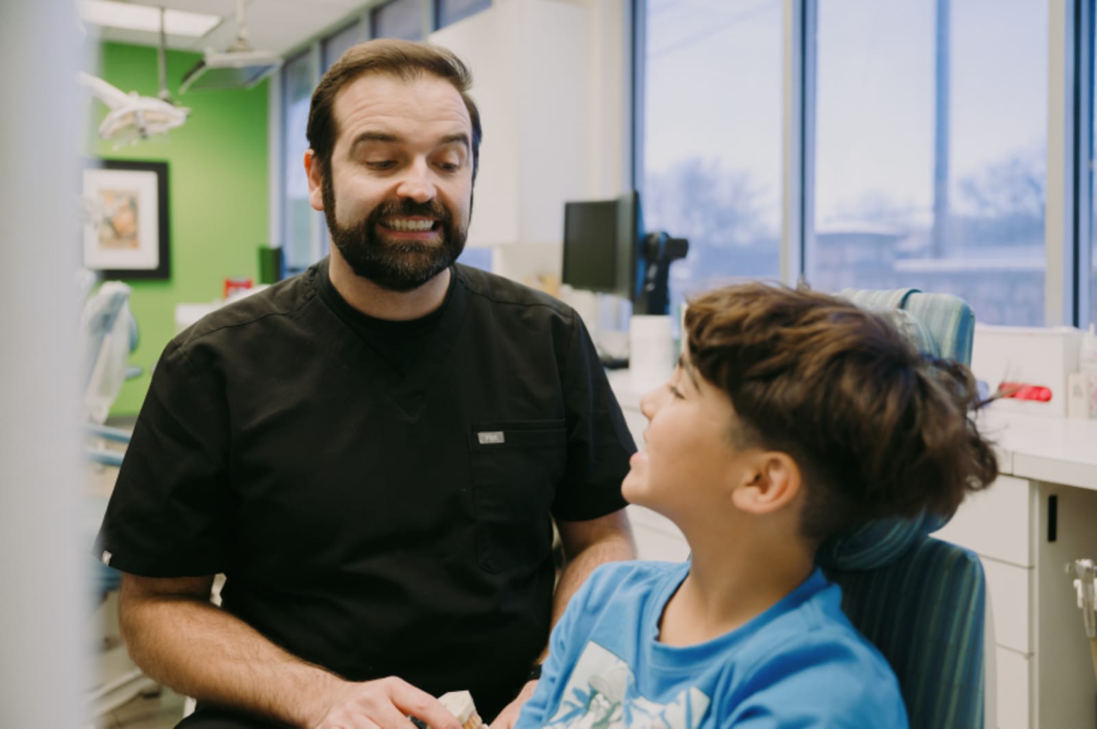 Male dentist speaking with young patient in clinical exam room setting