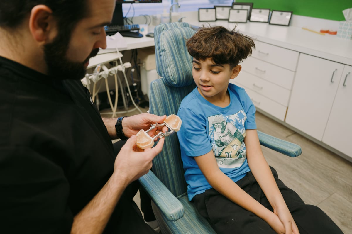 Pediatric dentist examining a young boy's teeth in a dental office treatment room.