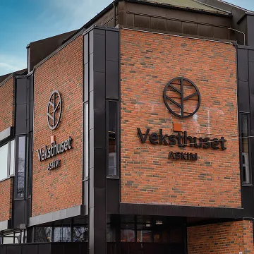 Exterior of a brick building with a black metal framed tree logo and the text 'Veksthuset Askim' on the wall.