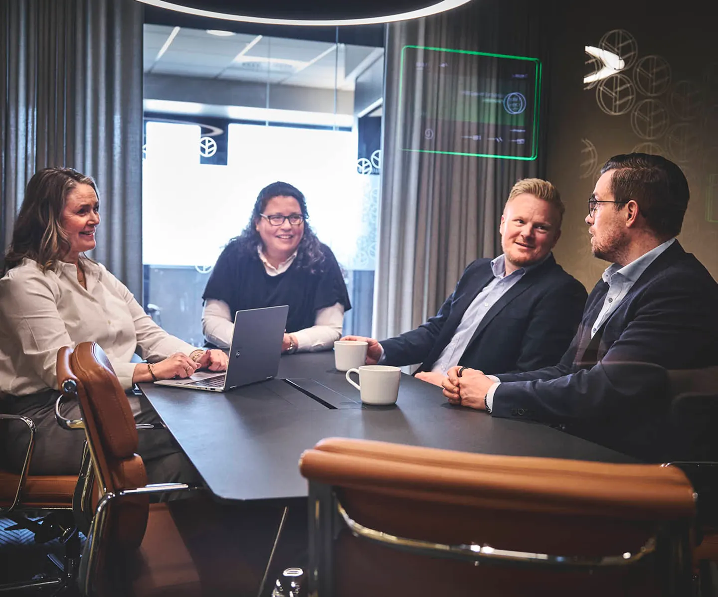Four business professionals sitting at a conference table having a discussion with coffee mugs and a laptop.