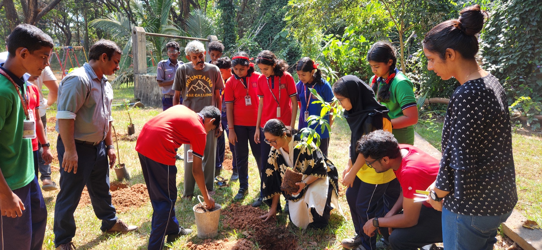 Green Kerala Volunteers participants gather around a young tree and plant it together.