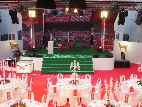 Bühnenbild mit grünem Teppich und Stadionausschnitte als Hintergrund