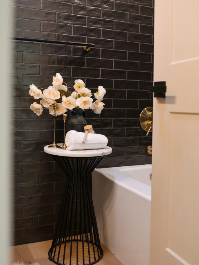 Alcove tub surrounded by glossy black subway tile with brass fixtures