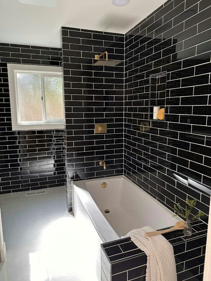 Shower over tub tiled in glossy black subway with a recessed niche