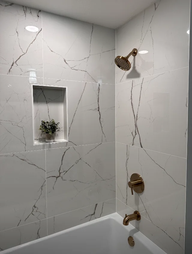 Tub and shower surround in white marble-look porcelain with a recessed niche and brass fixtures