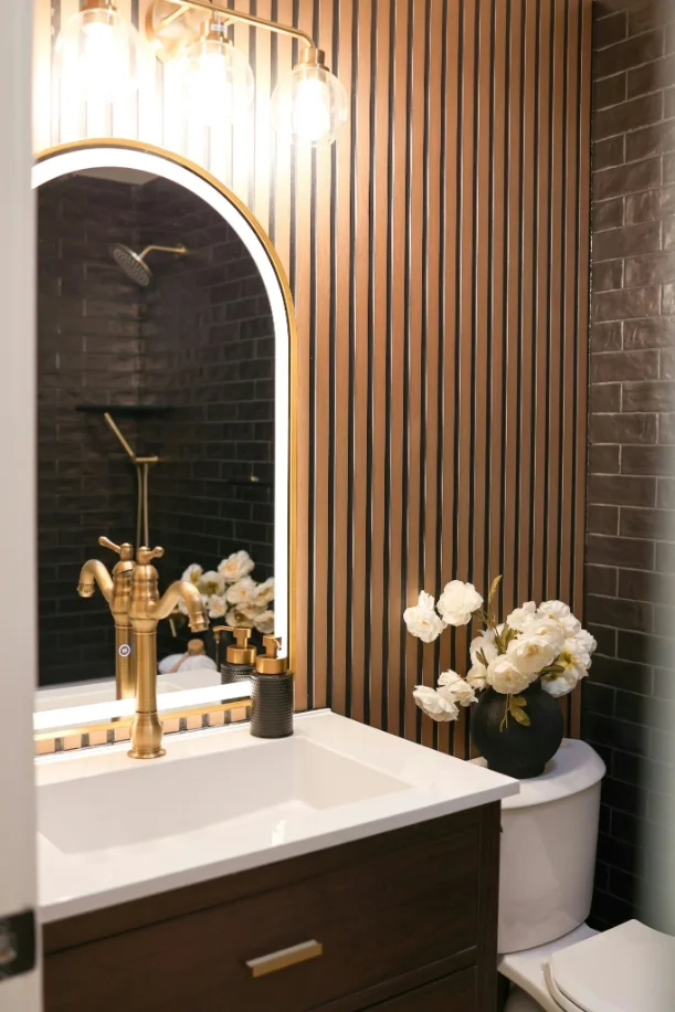 Powder room wall in dark espresso glazed brick tile beside a wood slat panel
