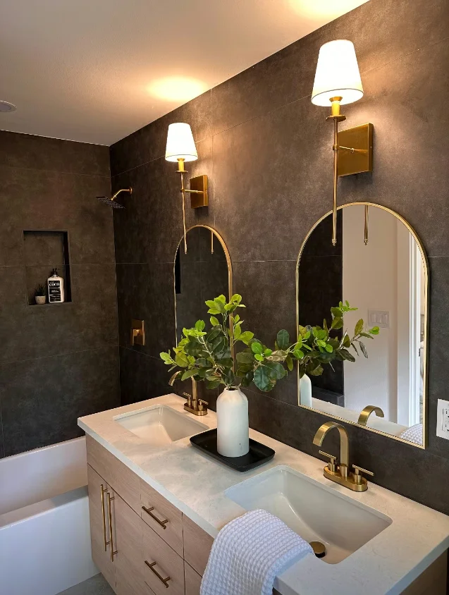 Bathroom in matte bronze large-format porcelain with an oak vanity and arched brass mirrors