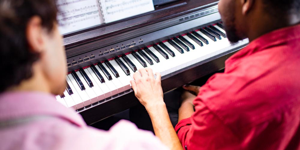 beginner learns to play the piano with music teacher
