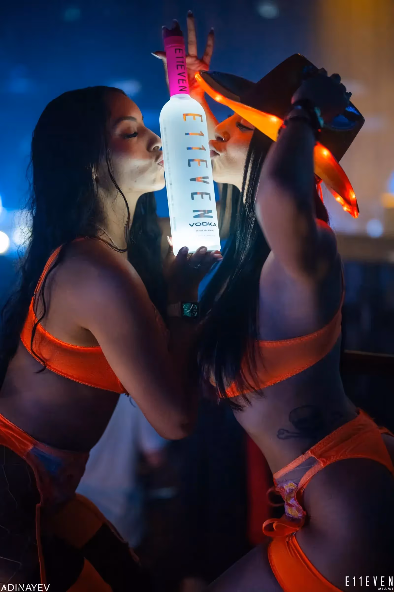 Two bottle girls kissing a bottle of E11EVEN vodka