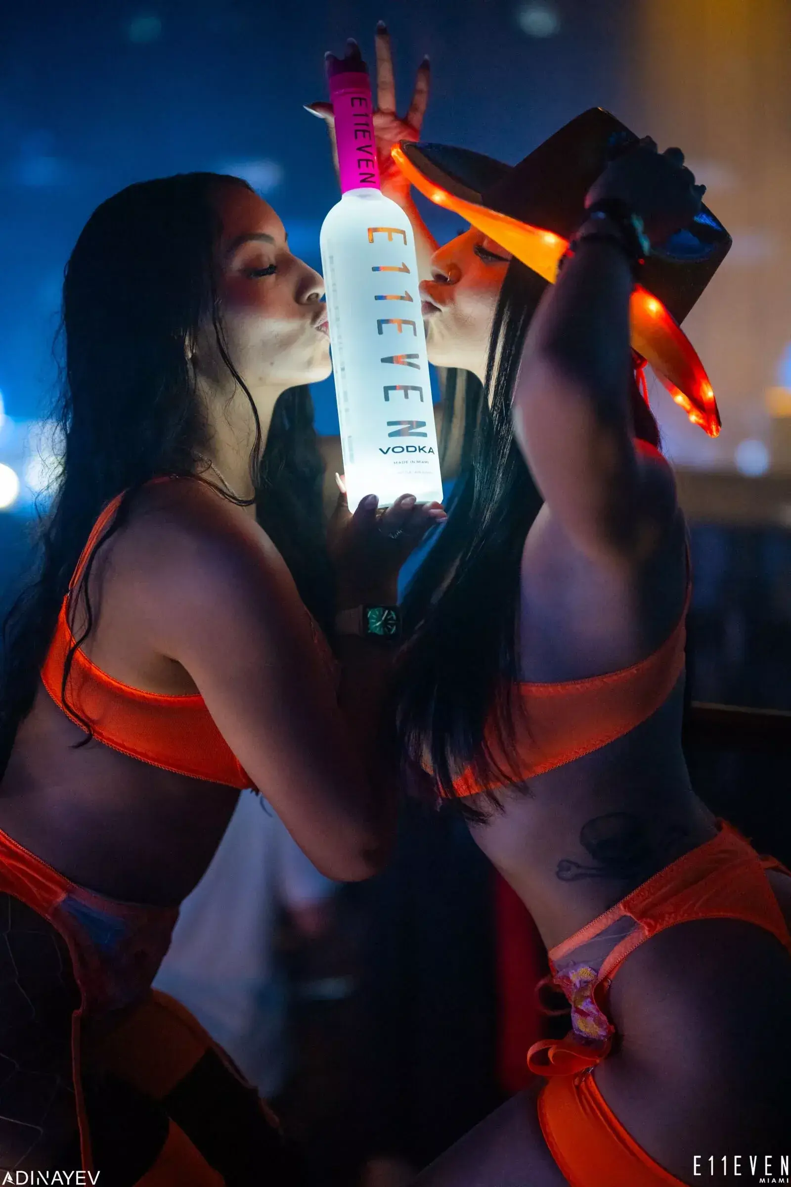 Two bottle girls kissing a bottle of E11EVEN vodka