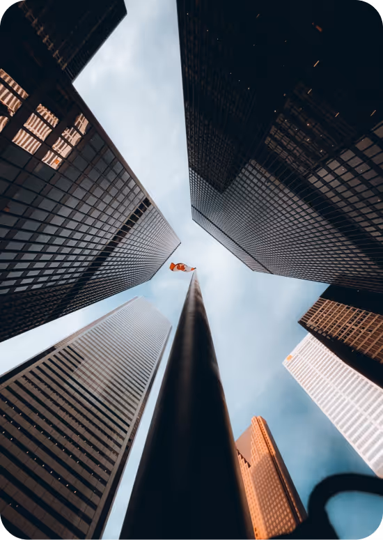 Looking up at tall skyscrapers surrounding a flagpole topped with a Canadian flag against a partly cloudy sky.