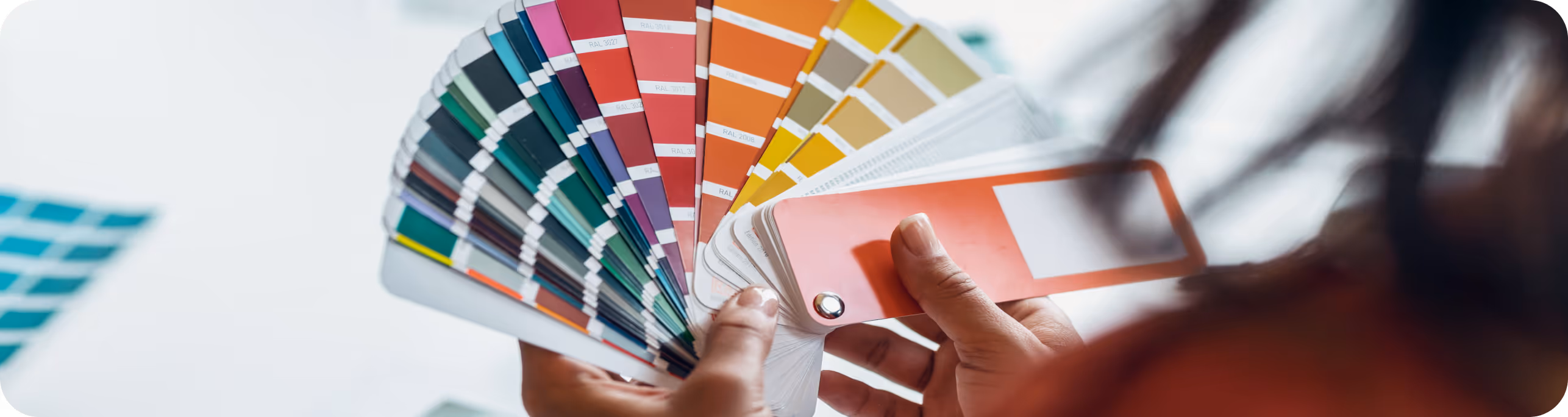 Person holding a fanned-out color swatch book showing various shades of blues, reds, oranges, and yellows.