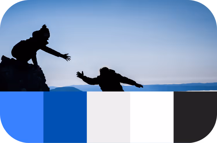 Silhouettes of two climbers reaching out to each other on a rocky mountain against a clear blue sky.
