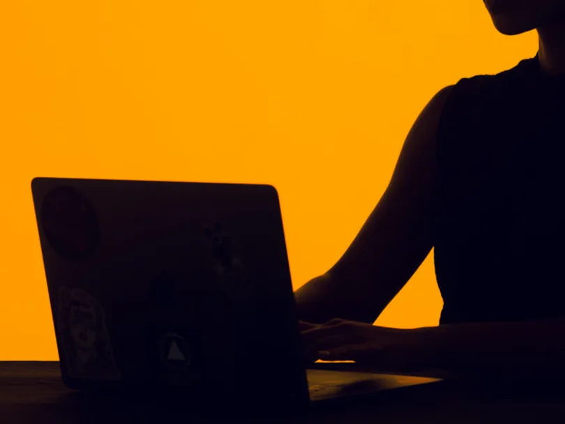 Silhouette of a woman working on a laptop against an orange wall