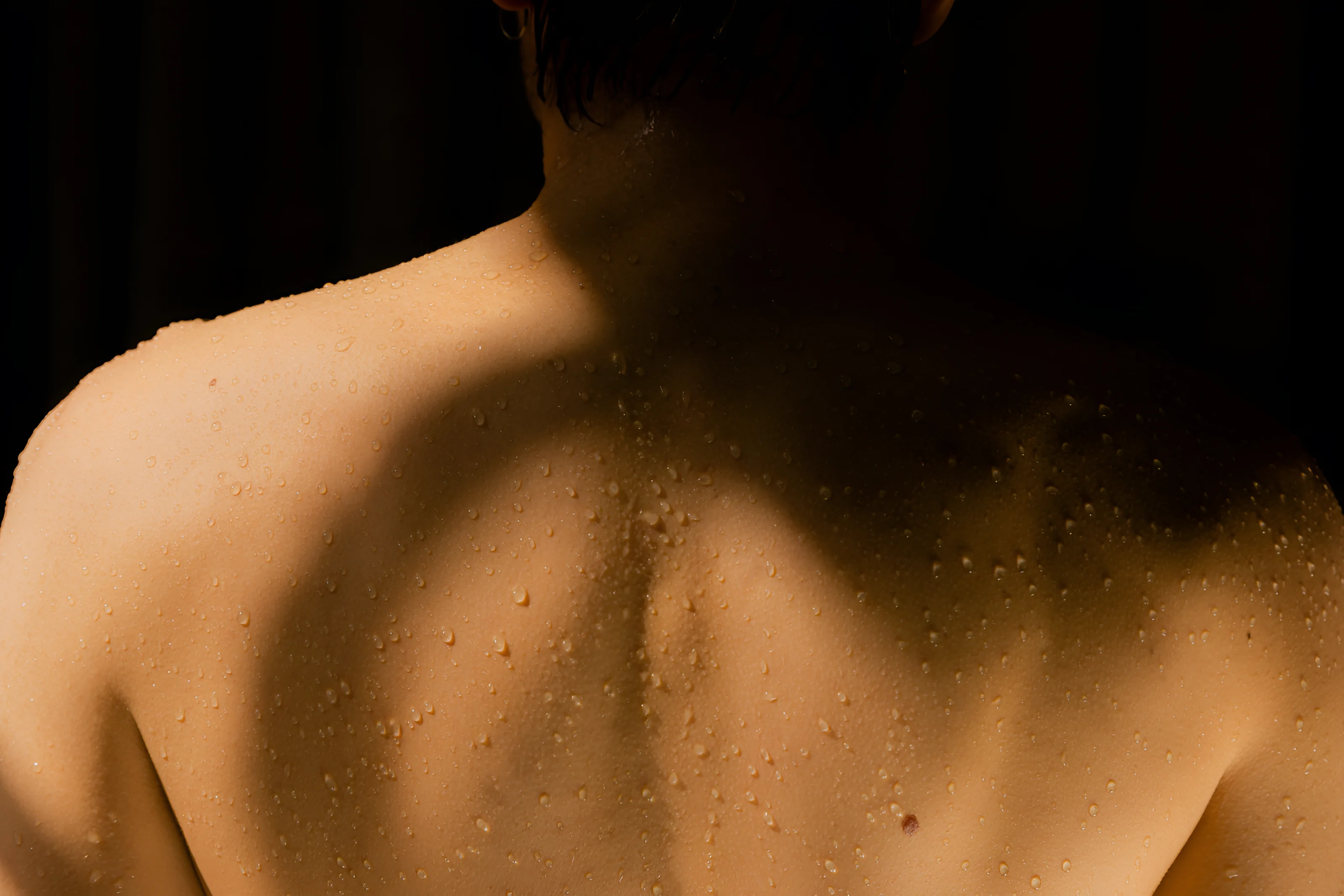 Close-up of a man's bare shoulder and neck with beads of sweat after a workout
