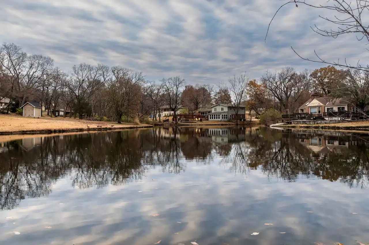 Lakeside homes reflected in a calm lake among bare trees