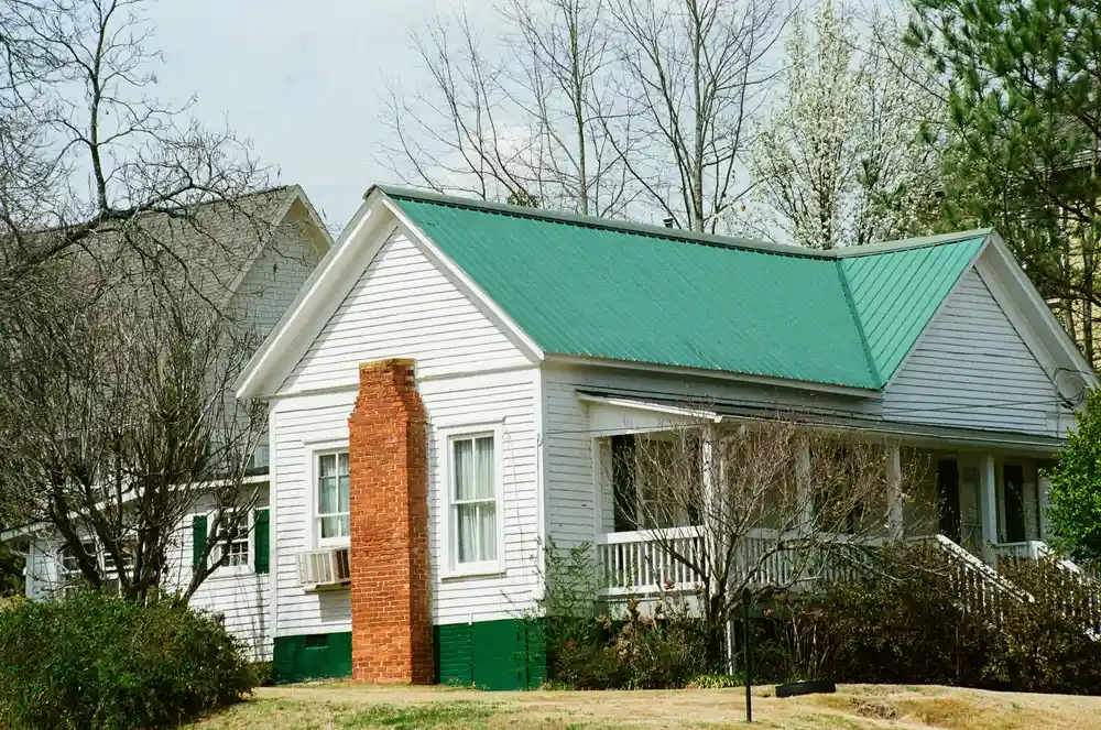 White single-family house with a green metal roof and brick chimney