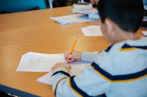 A young boy sitting at a table writing on a piece of paper