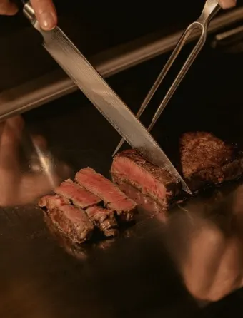 Reference photograph of a chef slicing grilled meat at a teppanyaki counter.