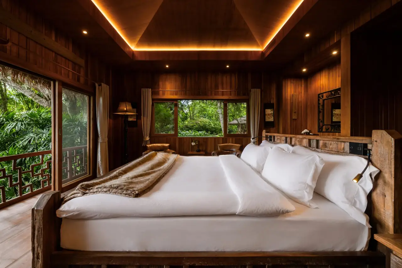 A villa bedroom with a softly lit timber ceiling, a large bed and a window onto the forest.