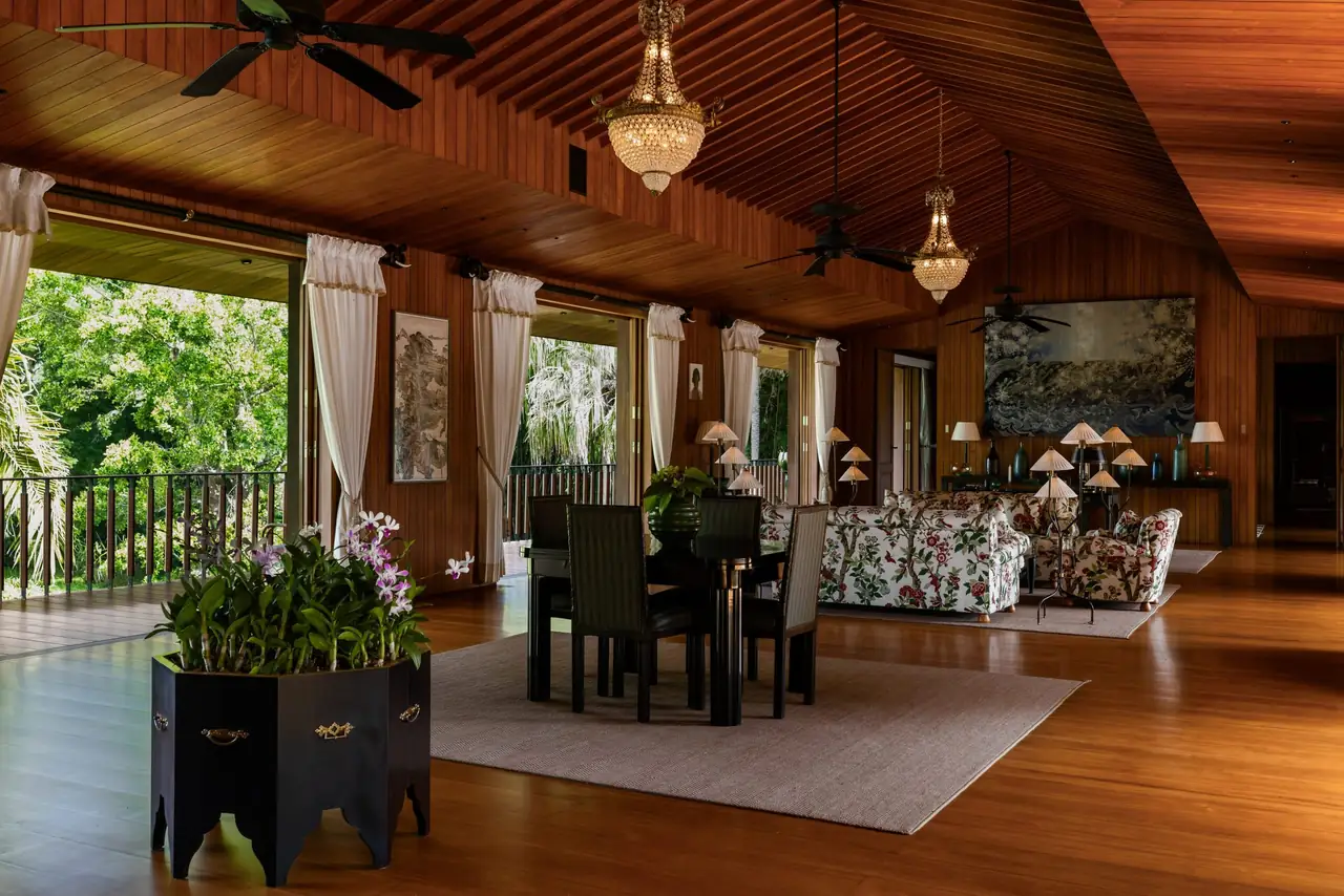 The great room: a vaulted timber ceiling with chandeliers, a dining table and floral sofas, with the garden beyond open doors.