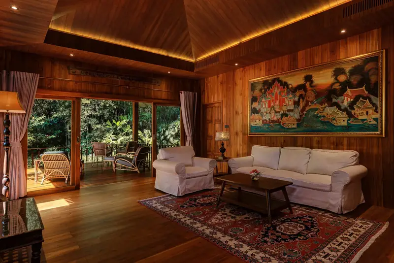 A living room with pale sofas, a Thai temple mural and doors open to the garden.