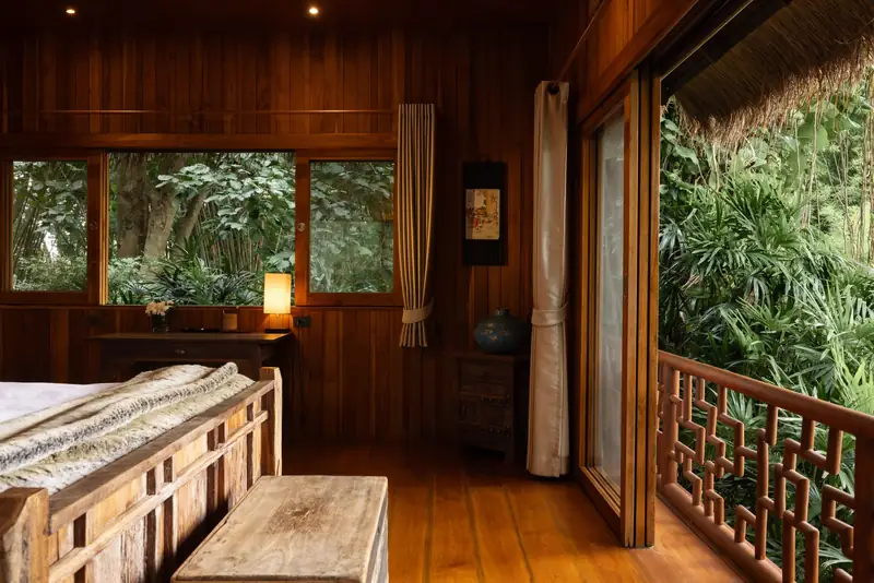 A bedroom corner with a window onto bamboo and a carved balcony screen.