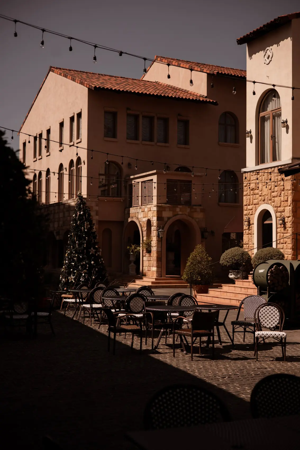 A courtyard of stone arches and terracotta, with café chairs, string lights and a Christmas tree.