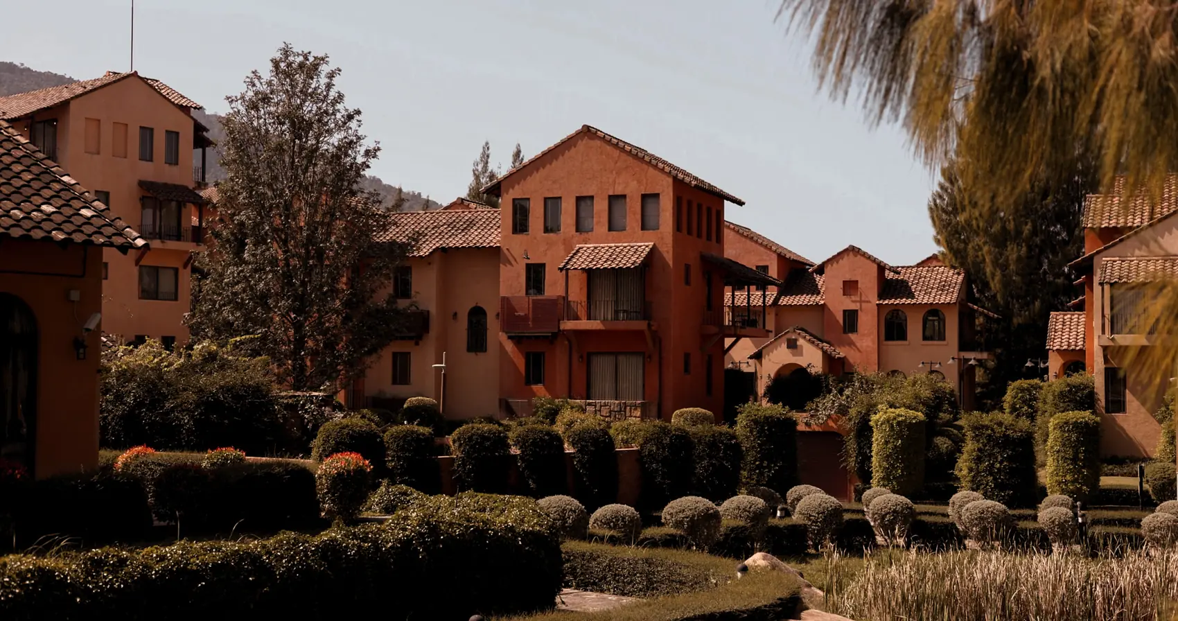 Terracotta villas set among clipped hedges, with the mountains behind.