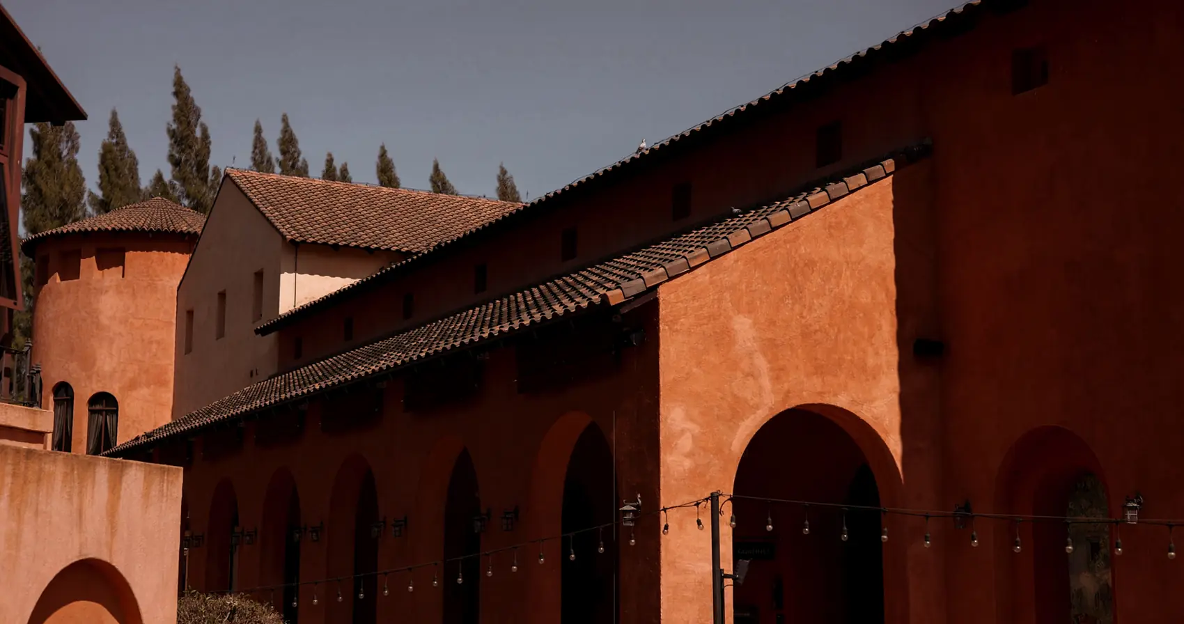 A long arcaded wall in terracotta stucco, with a round tower beyond.