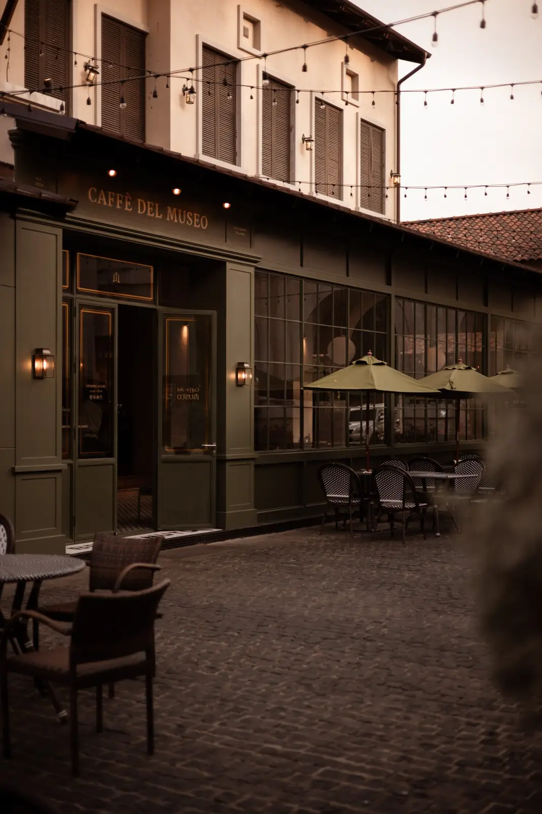 Caffè del Museo's green shopfront at dusk, with umbrellas and café chairs on the cobbles.