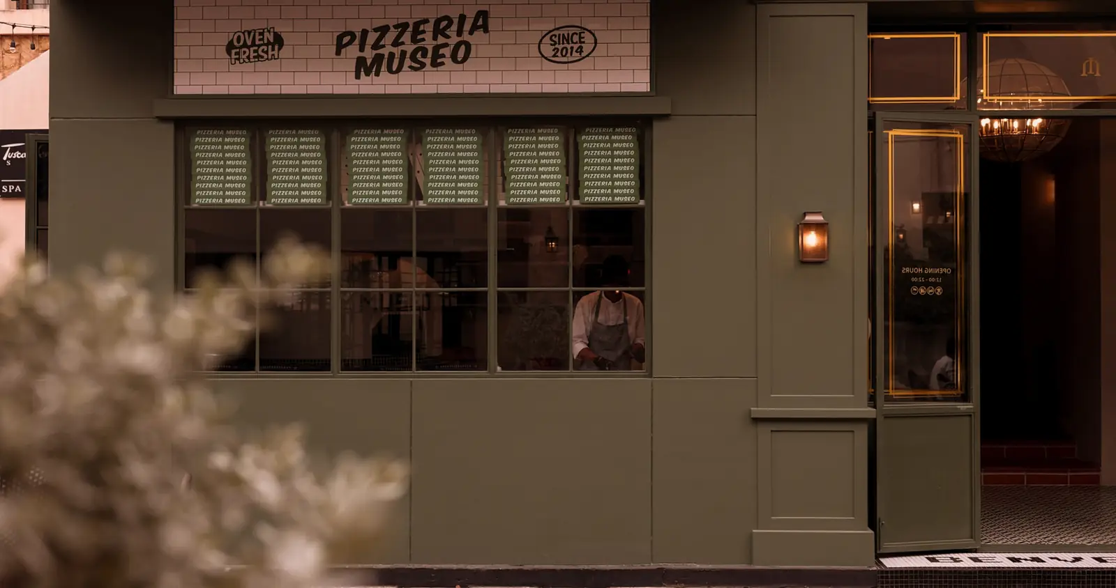 Pizzeria Museo's green window, with a cook at work inside.