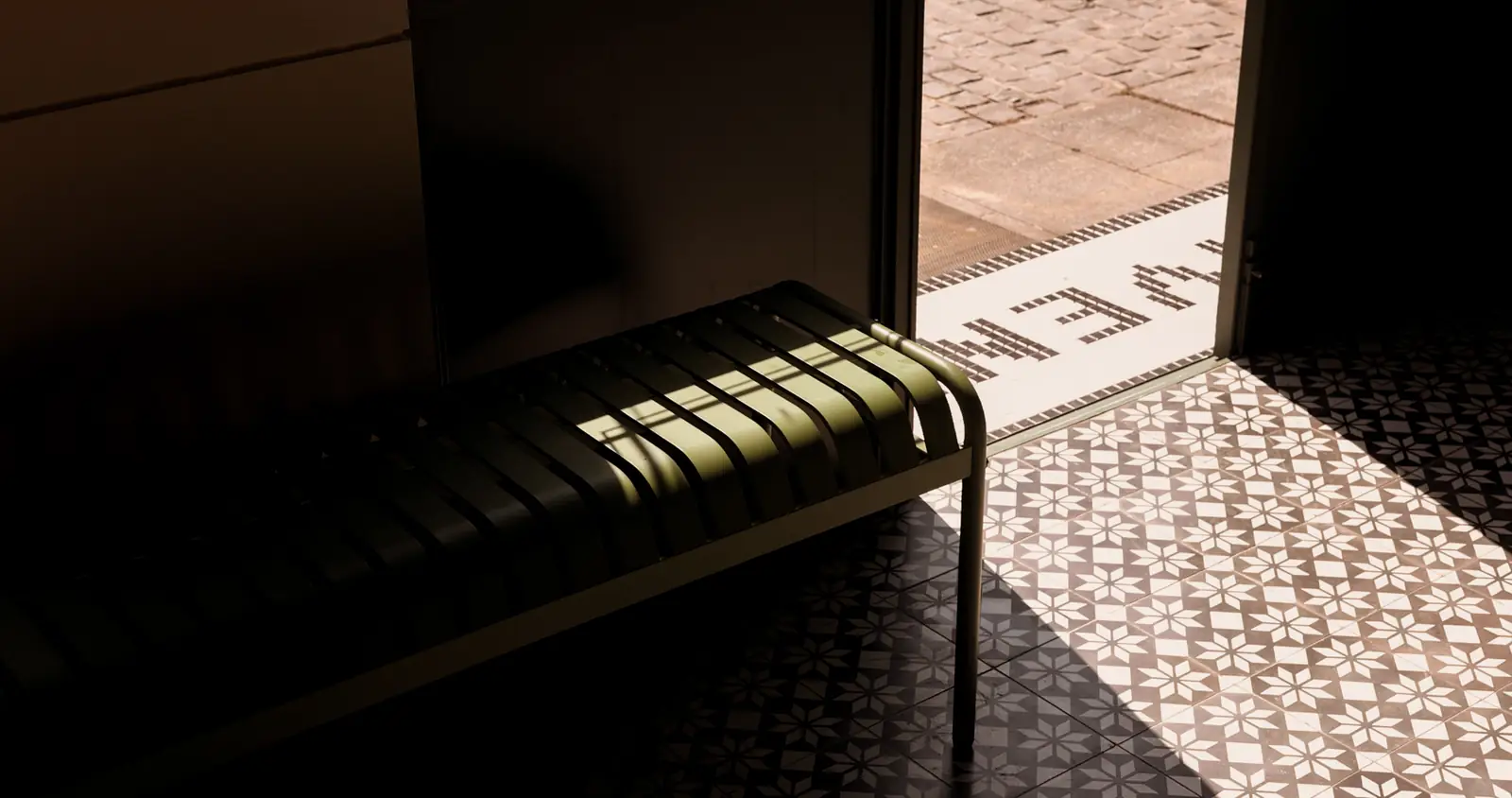 A slatted green bench beside the open door, with patterned tile in the light.