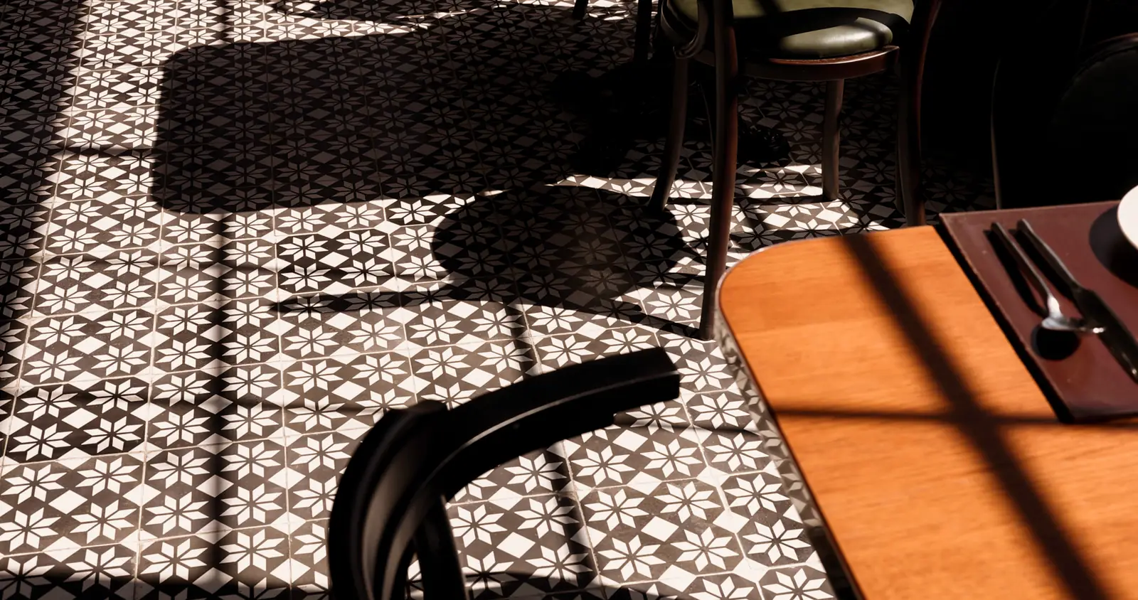 Patterned tile, a table setting and the shadows of chairs in the sun.