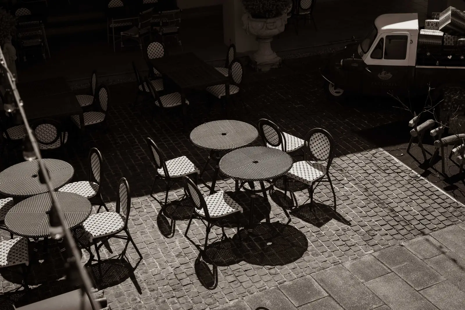 Round café tables and chairs on the cobbles, seen from above in monochrome.