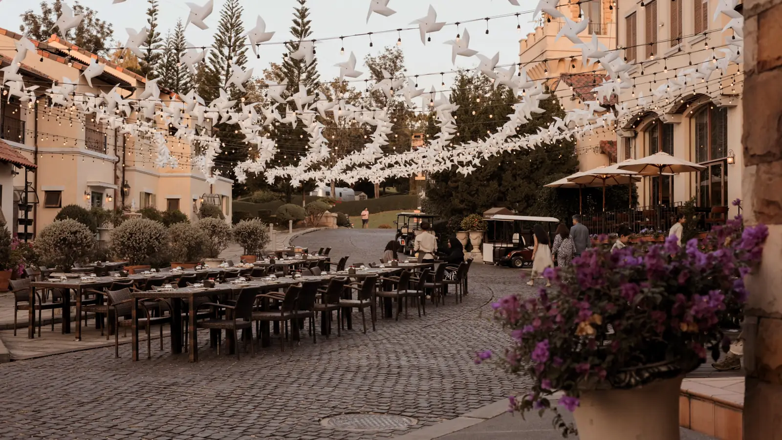 The street at dusk, with long tables laid and pinwheels strung overhead.