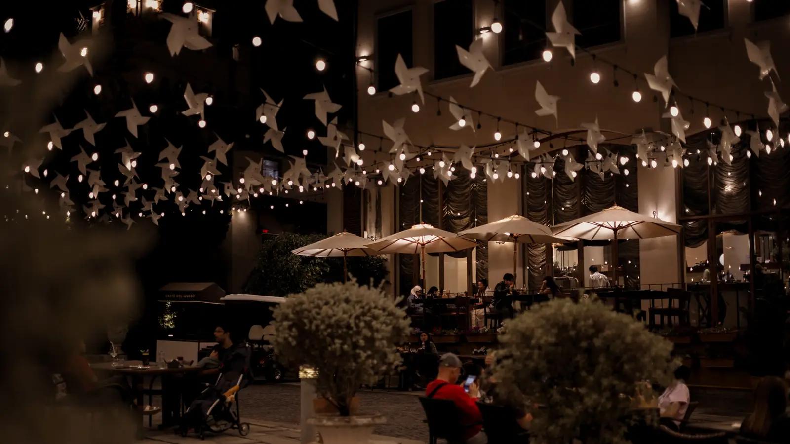 Diners under umbrellas at night, beneath pinwheels and string lights.