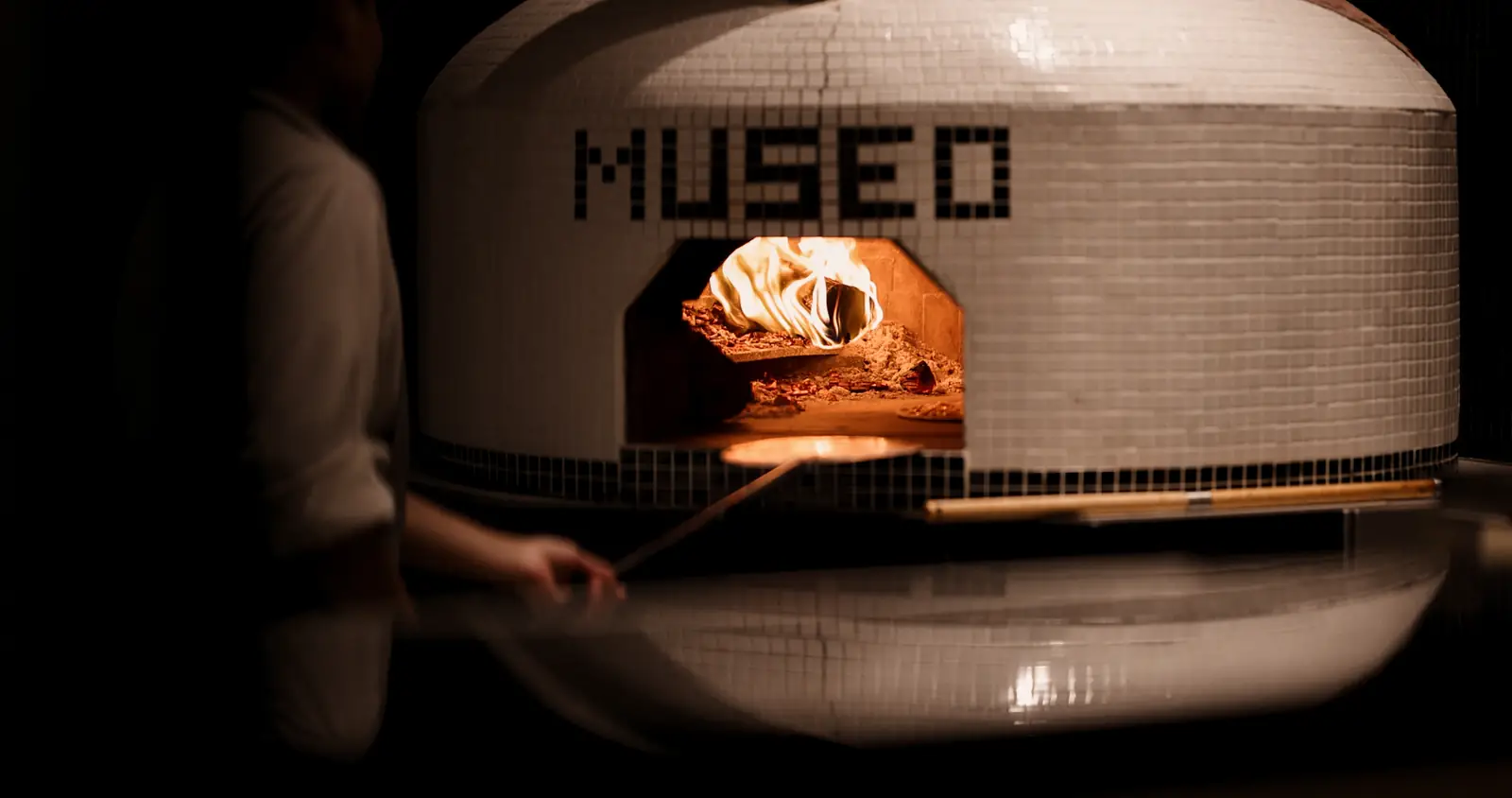The tiled pizza oven, lettered MUSEO, with a fire burning inside.