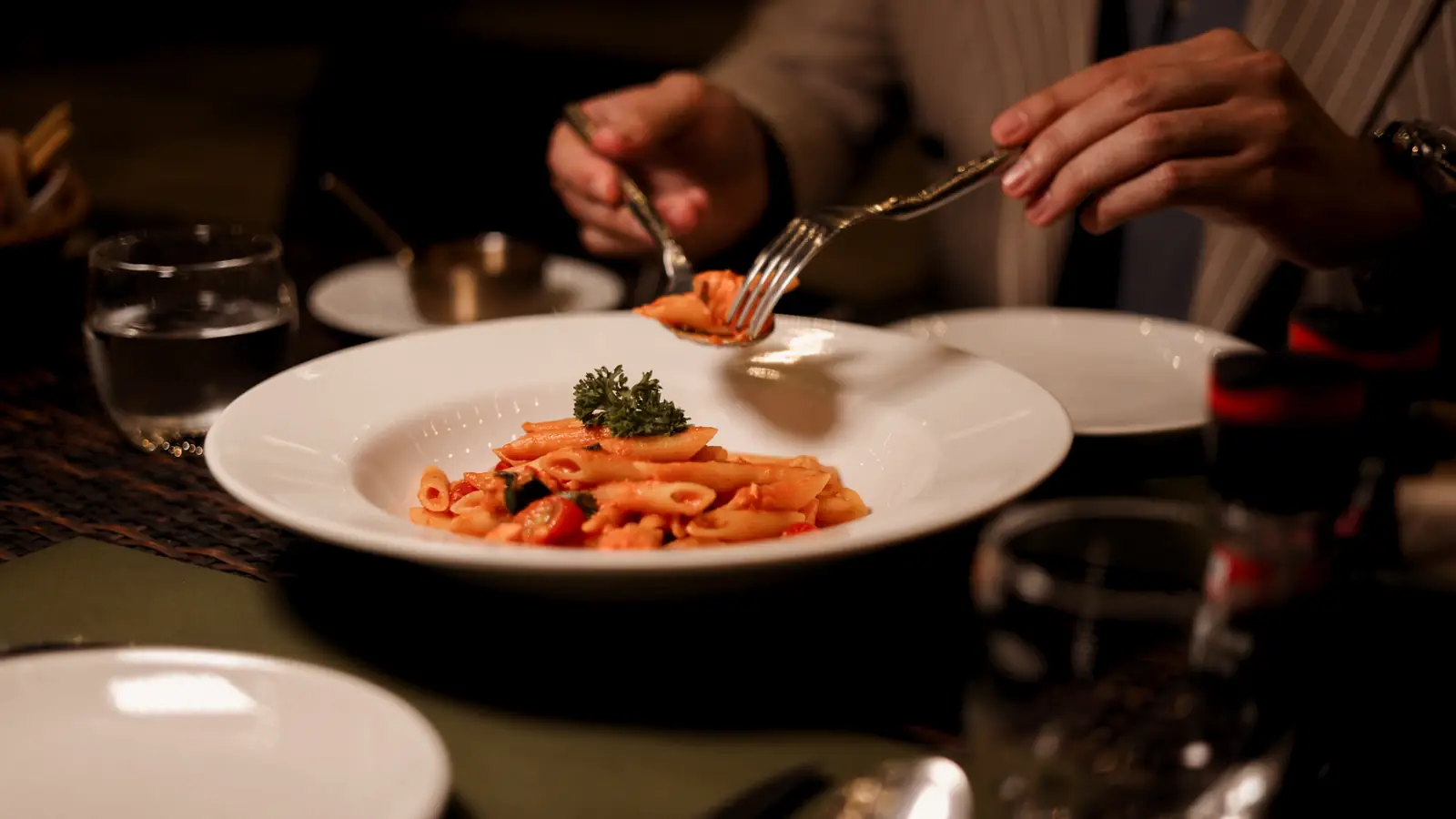Forking penne from a bowl of tomato pasta.